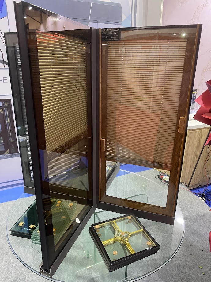A sample of a wood-look aluminum-framed glass door with curtains inside a glass display case is showcased on a round glass table.