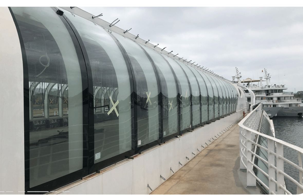 The curved glass walkway on the cruise ship features large glass walls overlooking the harbor.
