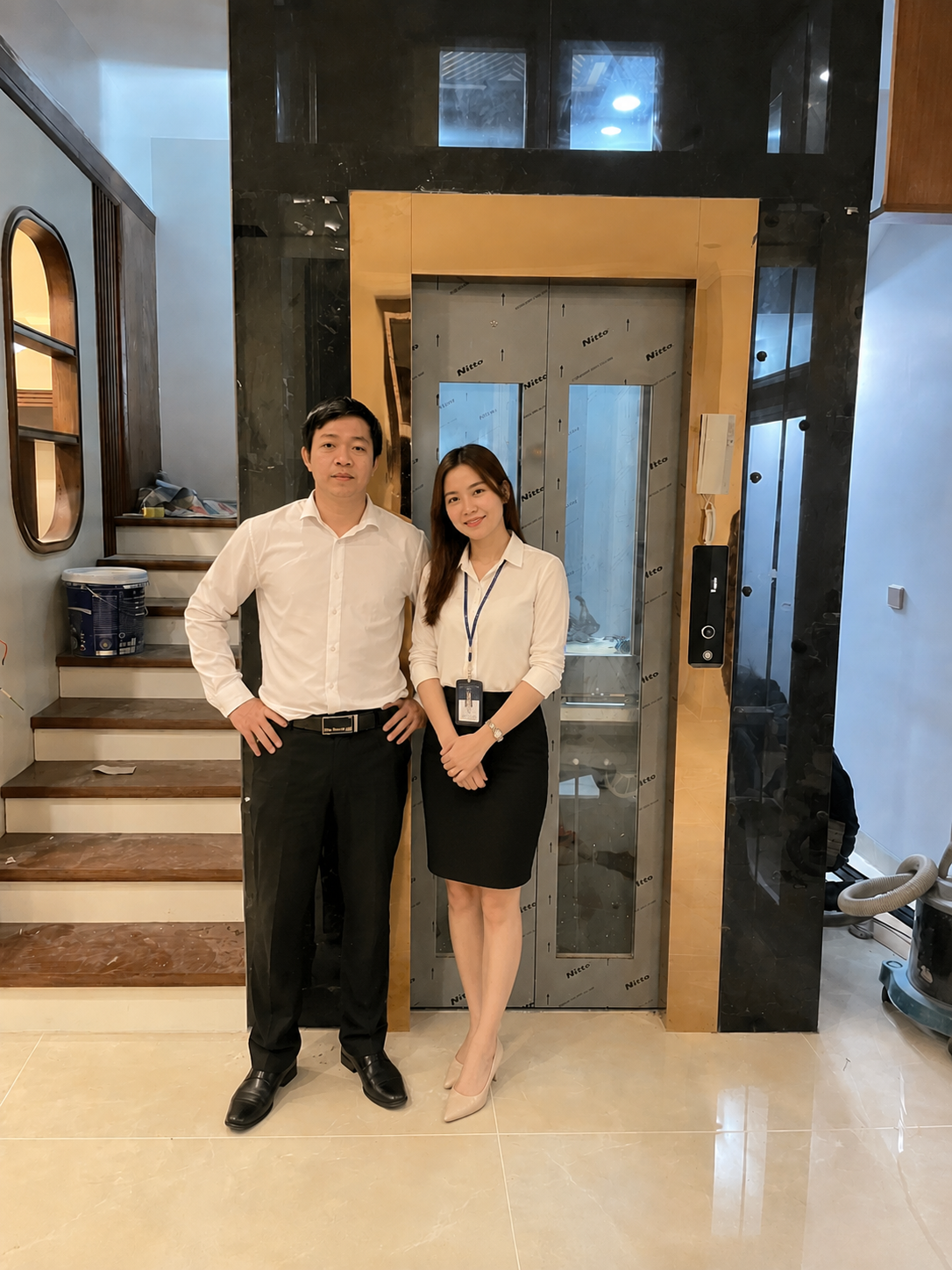 Two employees stand in front of a home elevator in a modern house undergoing interior finishing.