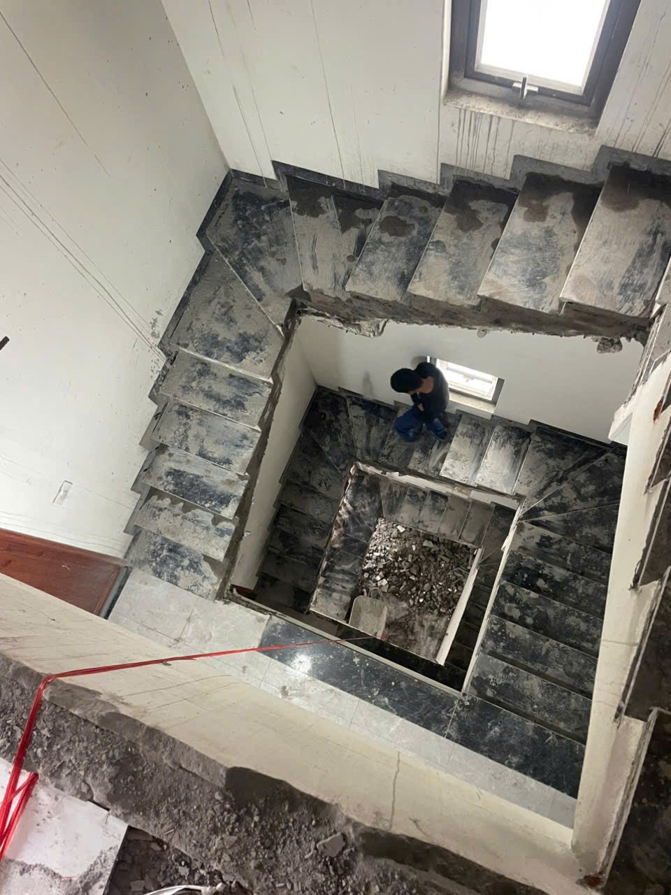 The concrete staircase is under construction, covered in dust and broken bricks, with workers walking around inspecting the site.