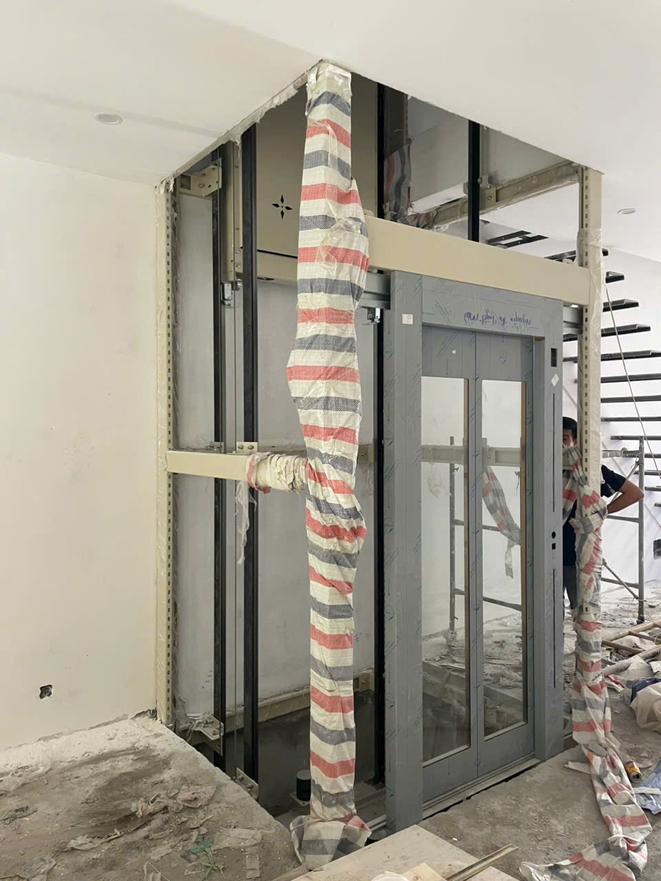 Installation of a glass-framed home elevator and landing doors is nearing completion in a newly constructed building.