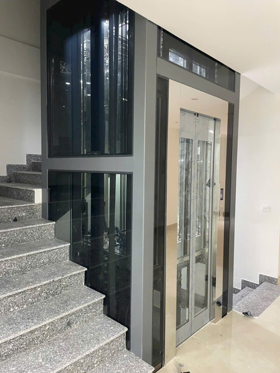 Modern home elevator with glass walls and stainless steel frame, installed next to the staircase.
