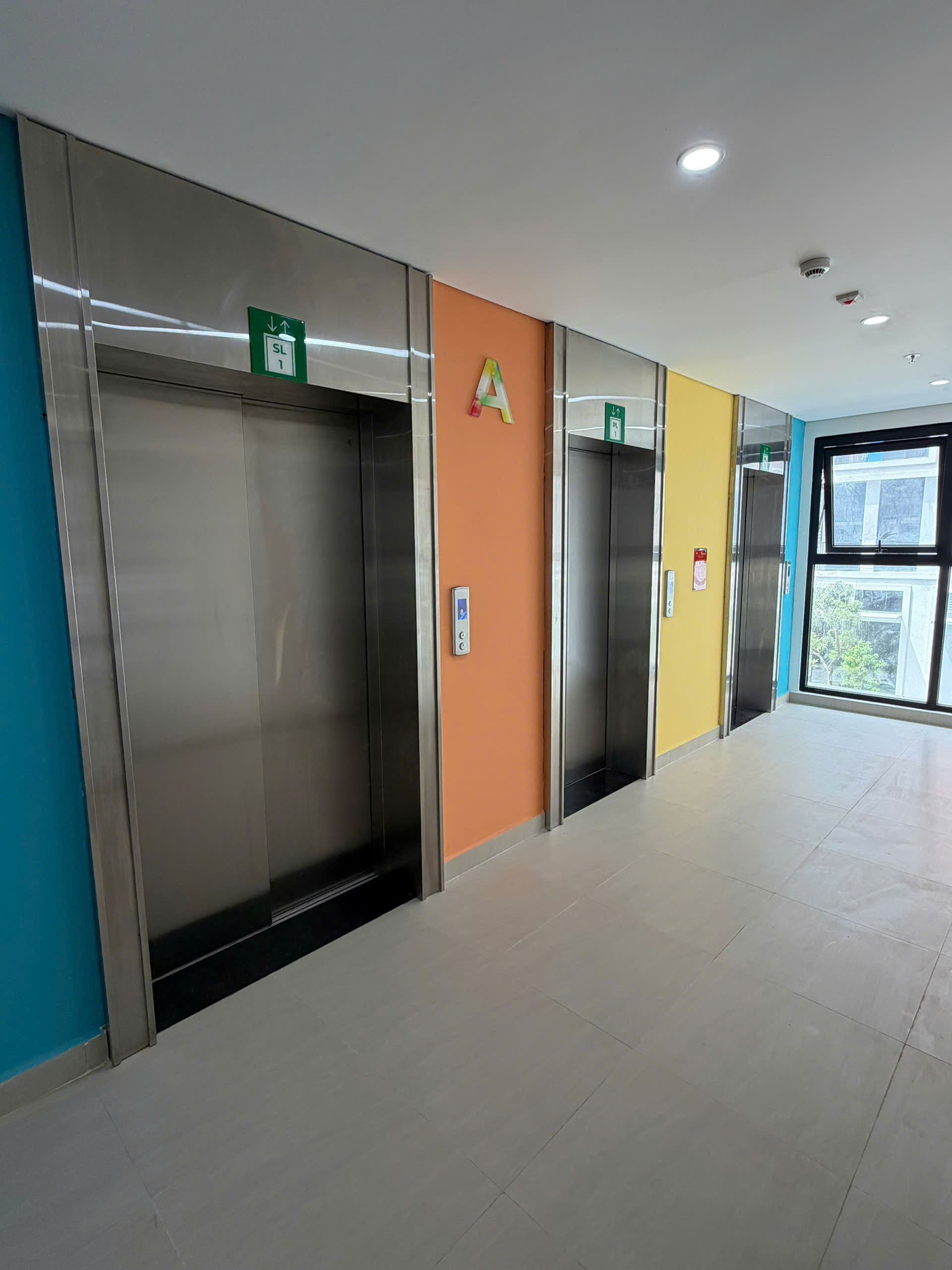 Cụm ba thang máy cửa inox trong hành lang tòa nhà với tường nhiều màu sáng