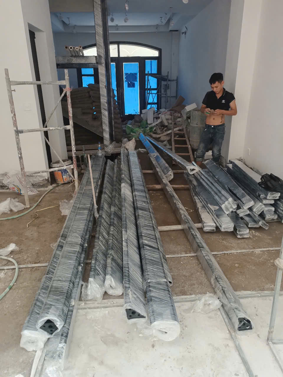 Aluminum profiles wrapped in plastic film are stacked on the floor at an interior construction site.