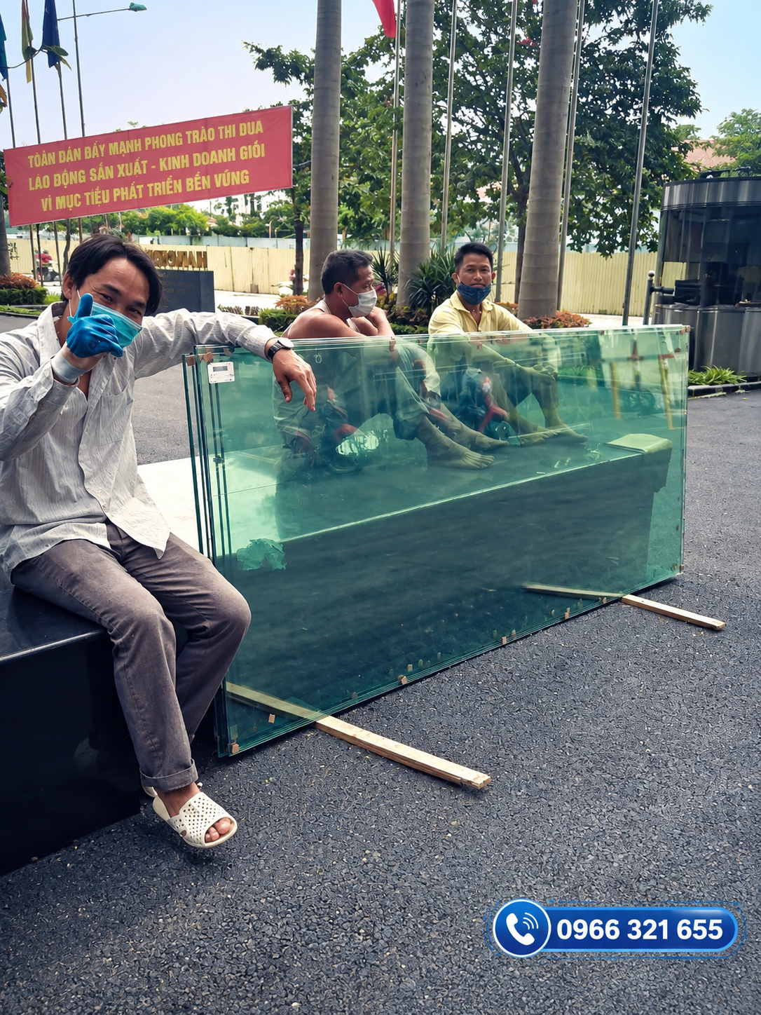 Bể kính lớn màu xanh được trưng bày ngoài trời, phía sau kính có người ngồi bên trong 񟿿
