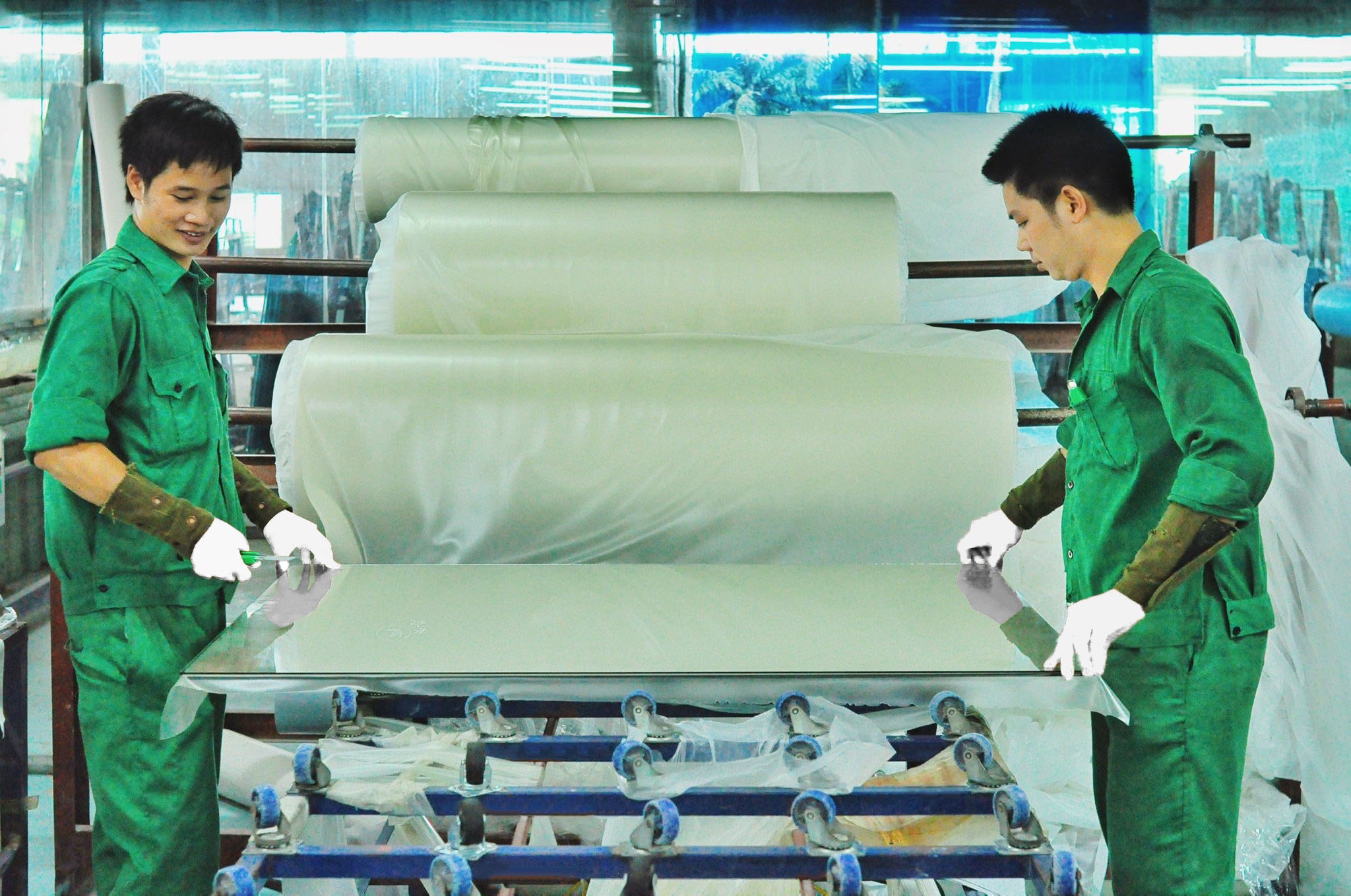 Các tấm vật liệu dạng màng màu trắng được công nhân xử lý trên băng chuyền trong nhà máy