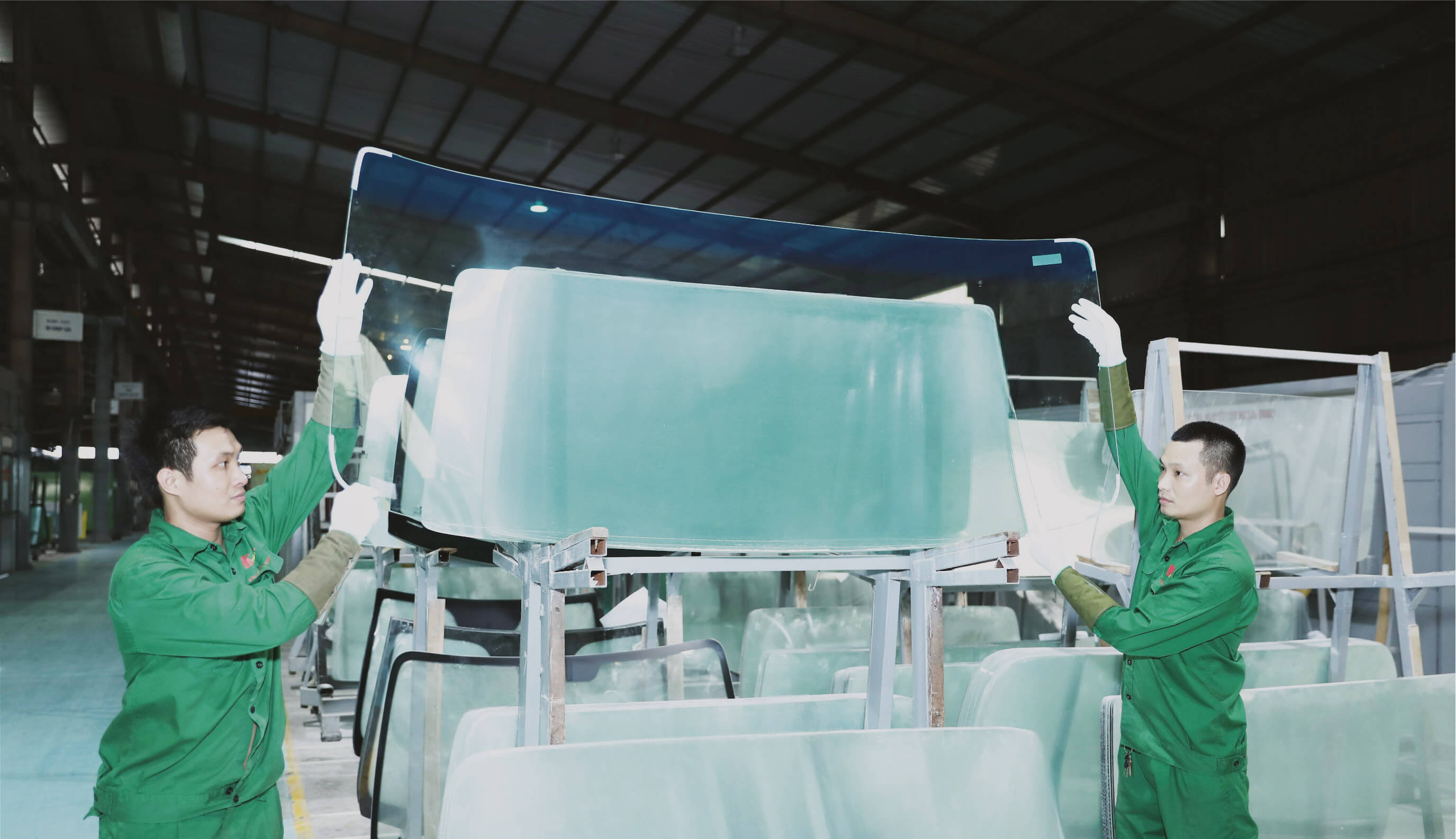 Hai nhân viên nâng giữ tấm kính lớn trong nhà xưởng