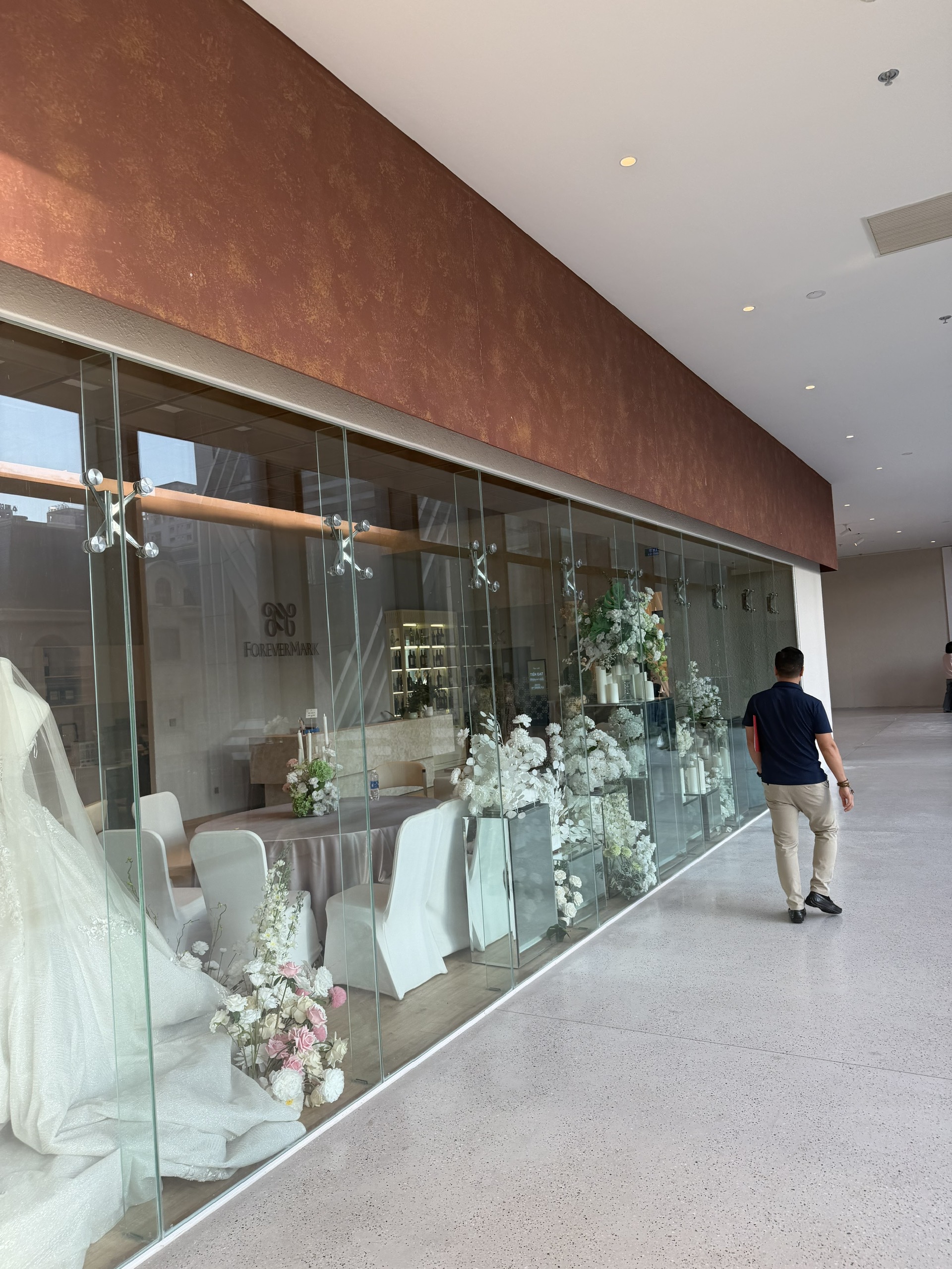 Cửa hàng trang trí cưới với váy cưới trắng trưng bày sau vách kính và bàn ghế phủ khăn sang trọng