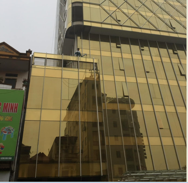 Cleaning staff use safety harnesses to clean the glass facade of a gold-colored high-rise building.