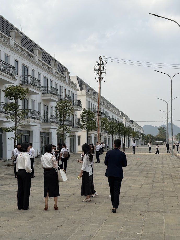 Nhân viên văn phòng tập trung trên vỉa hè trước dãy nhà phố thương mại trắng nhiều tầng