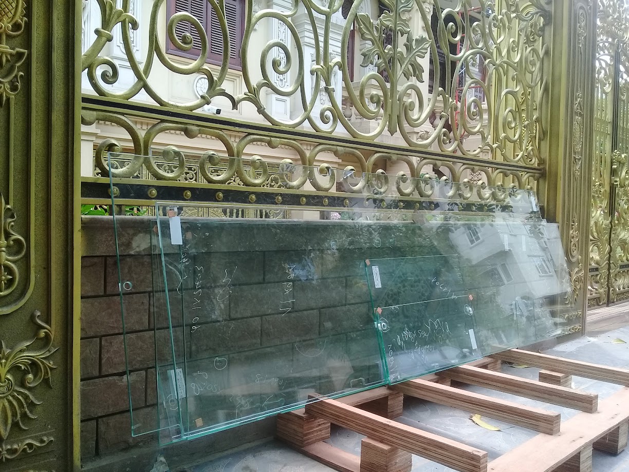 Tấm kính cường lực đặt trên giá gỗ trước cổng sắt hoa văn màu vàng của biệt thự